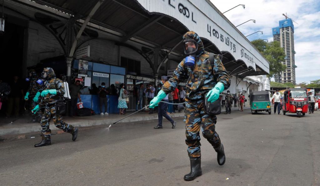 Sri Lankan government soldiers in protective clothes spray disinfectants at a railway station